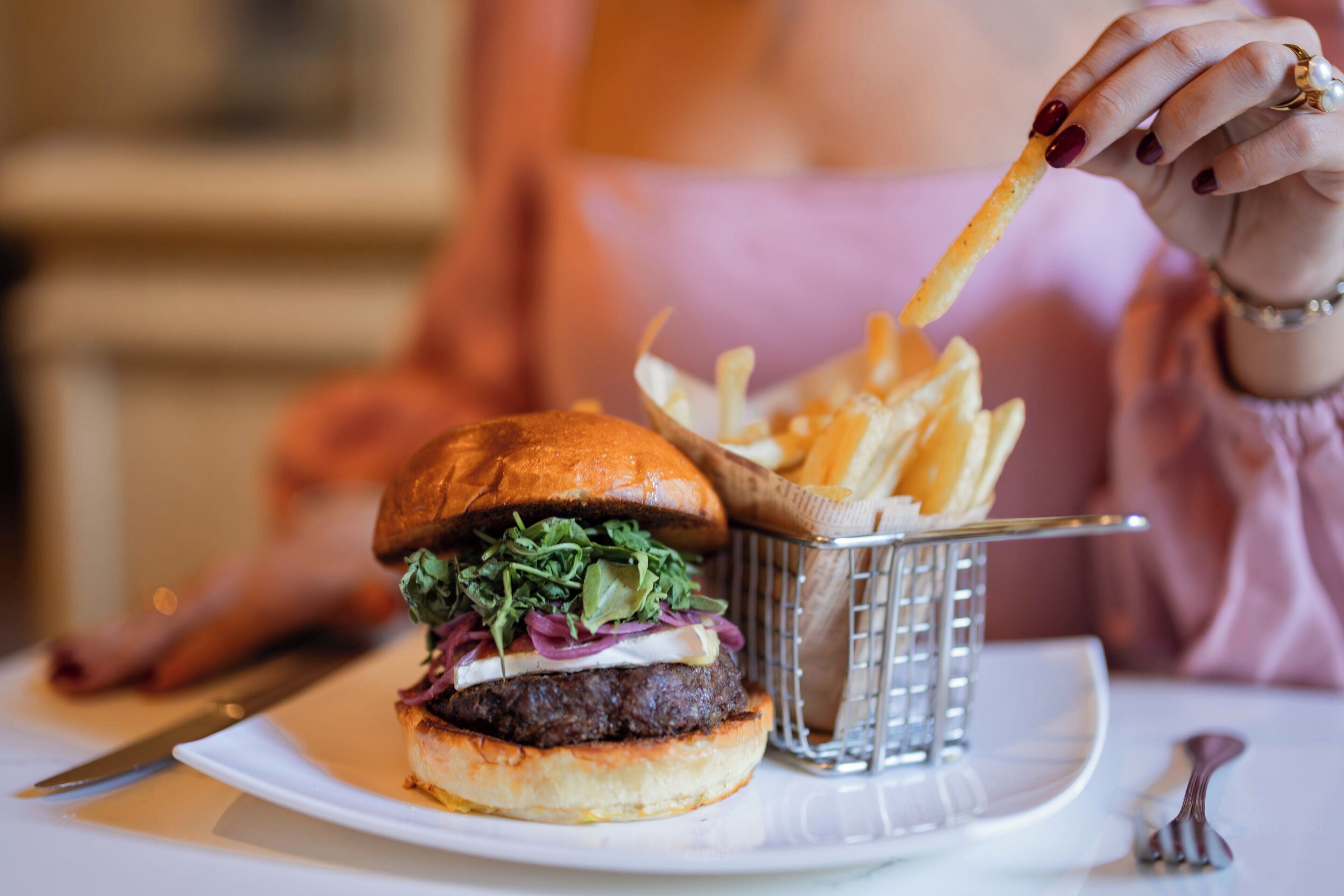 A burger with lettuce and red onions, a basket of fries, and a fork on a plate.