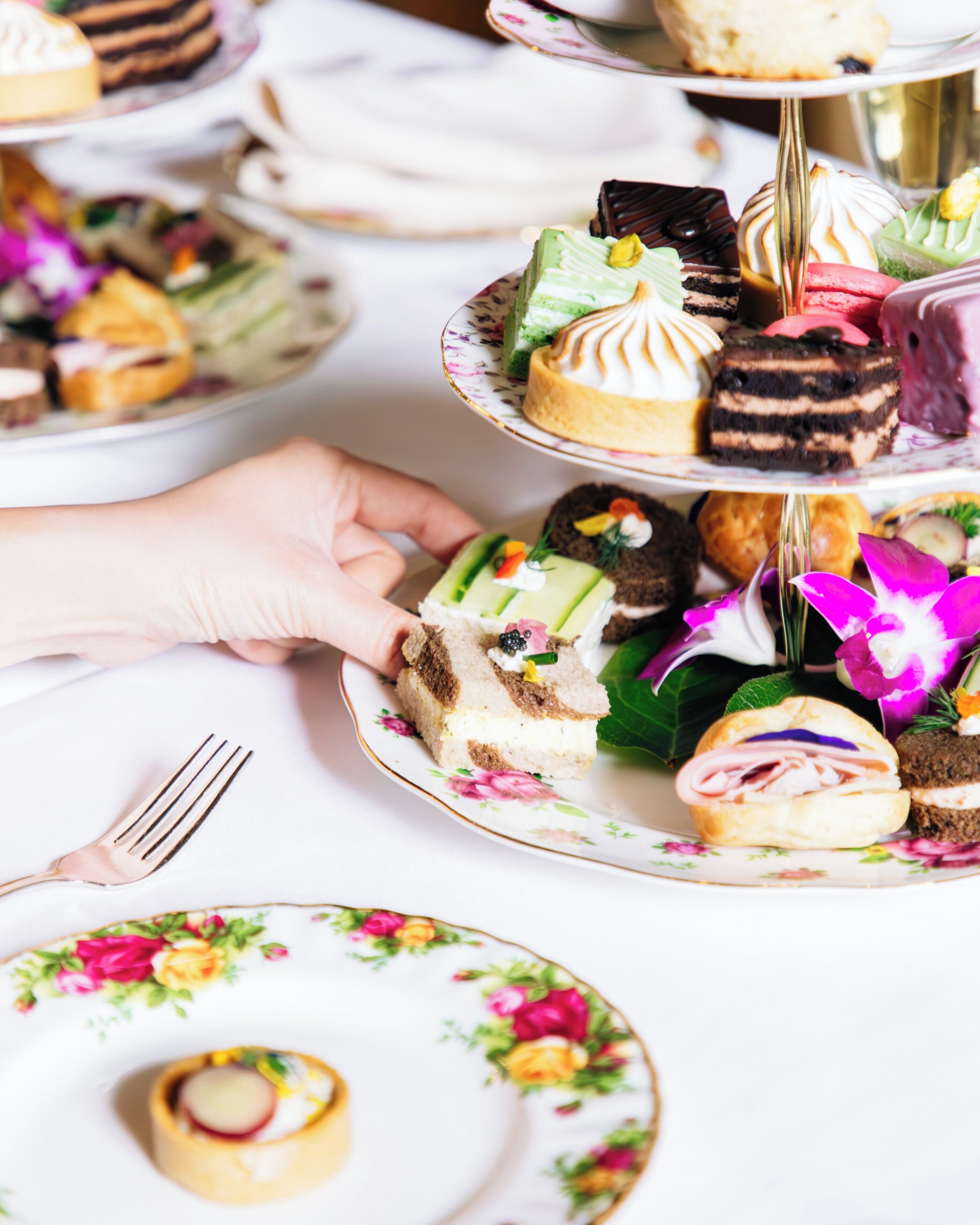 Exhibición escalonada de postres con diversas pastelerías y una mano alcanzando un trozo.