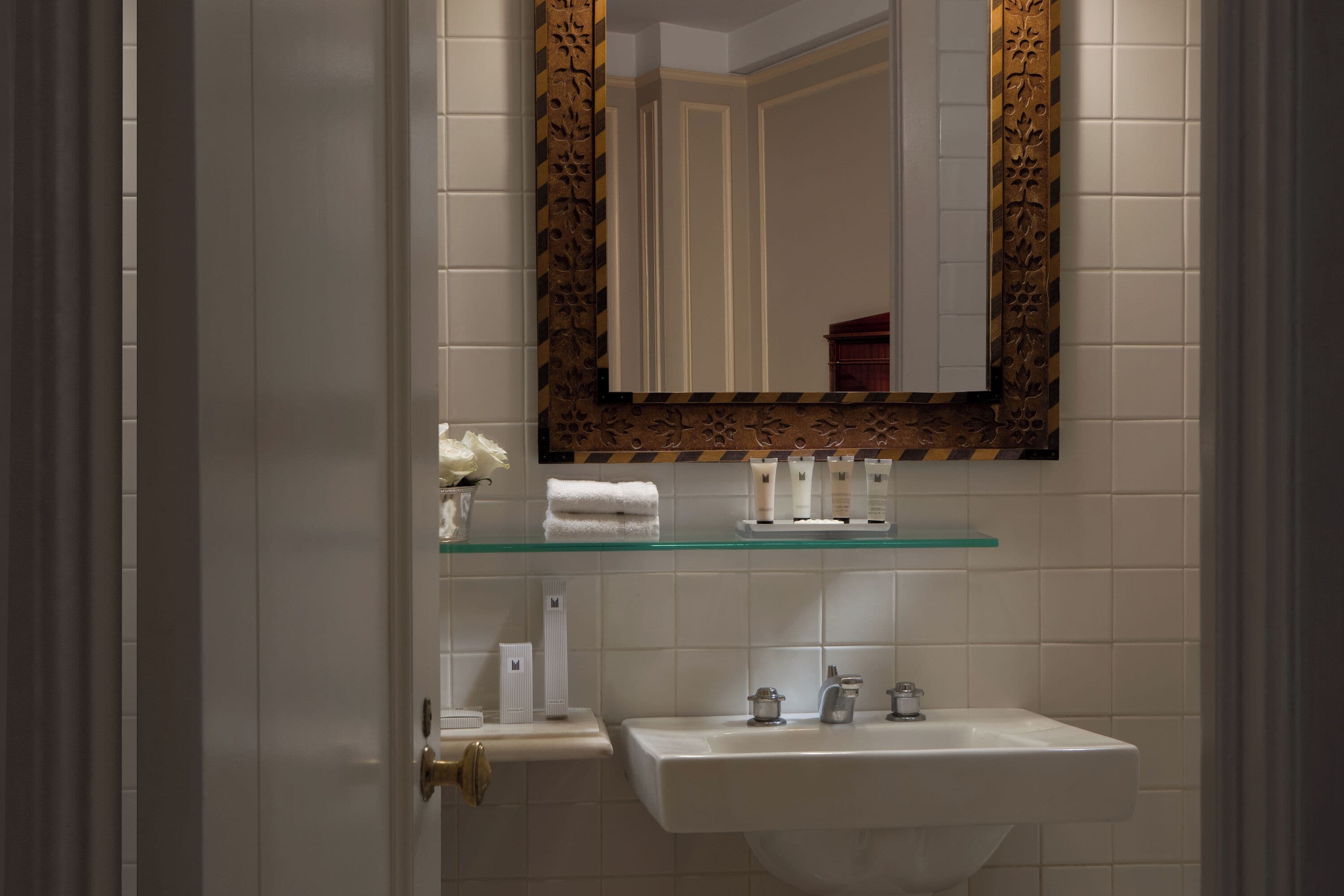 A bathroom with a white sink, a mirror with a decorative frame, and toiletries on a shelf.