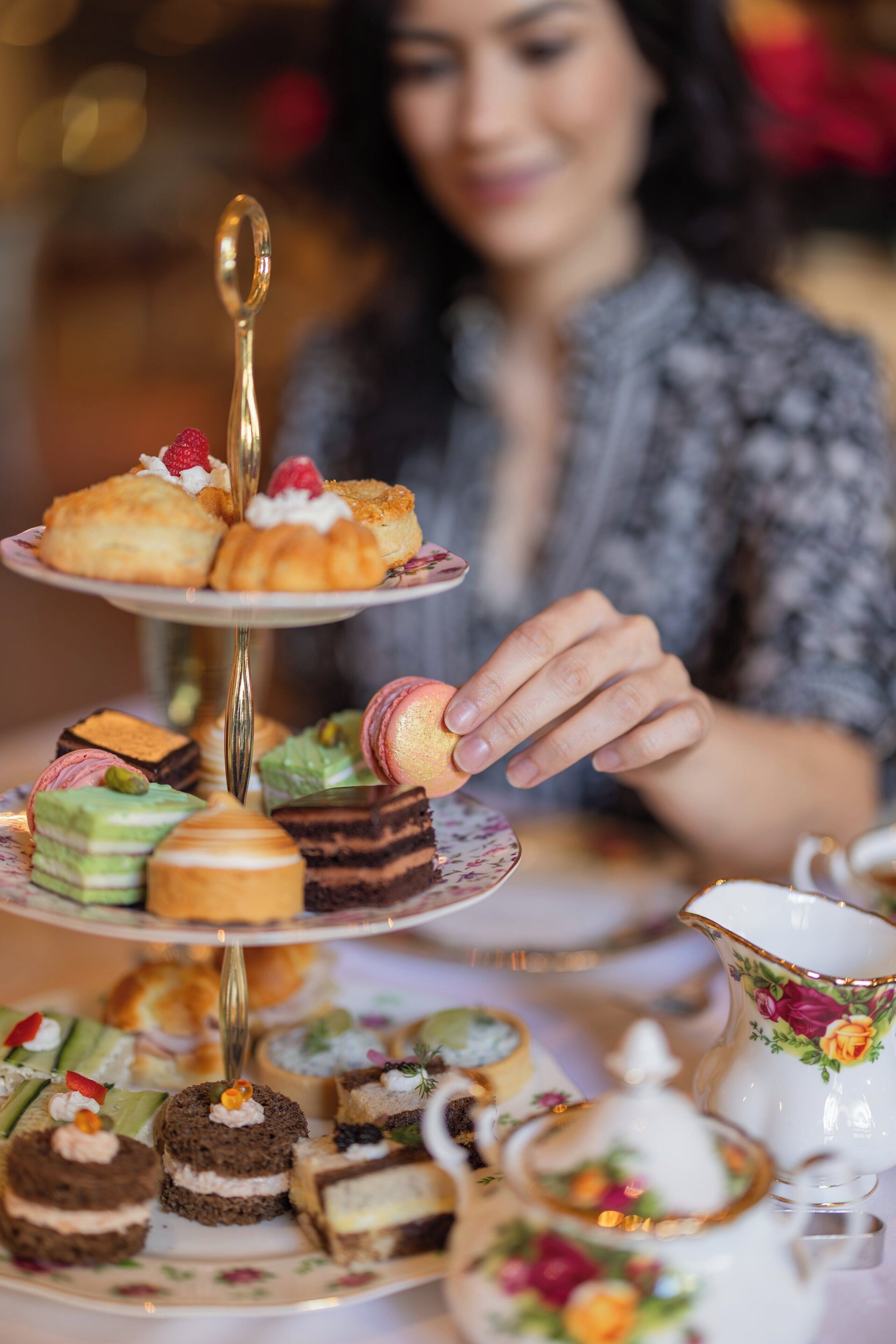 A tiered dessert stand with various pastries and a teapot on a table.