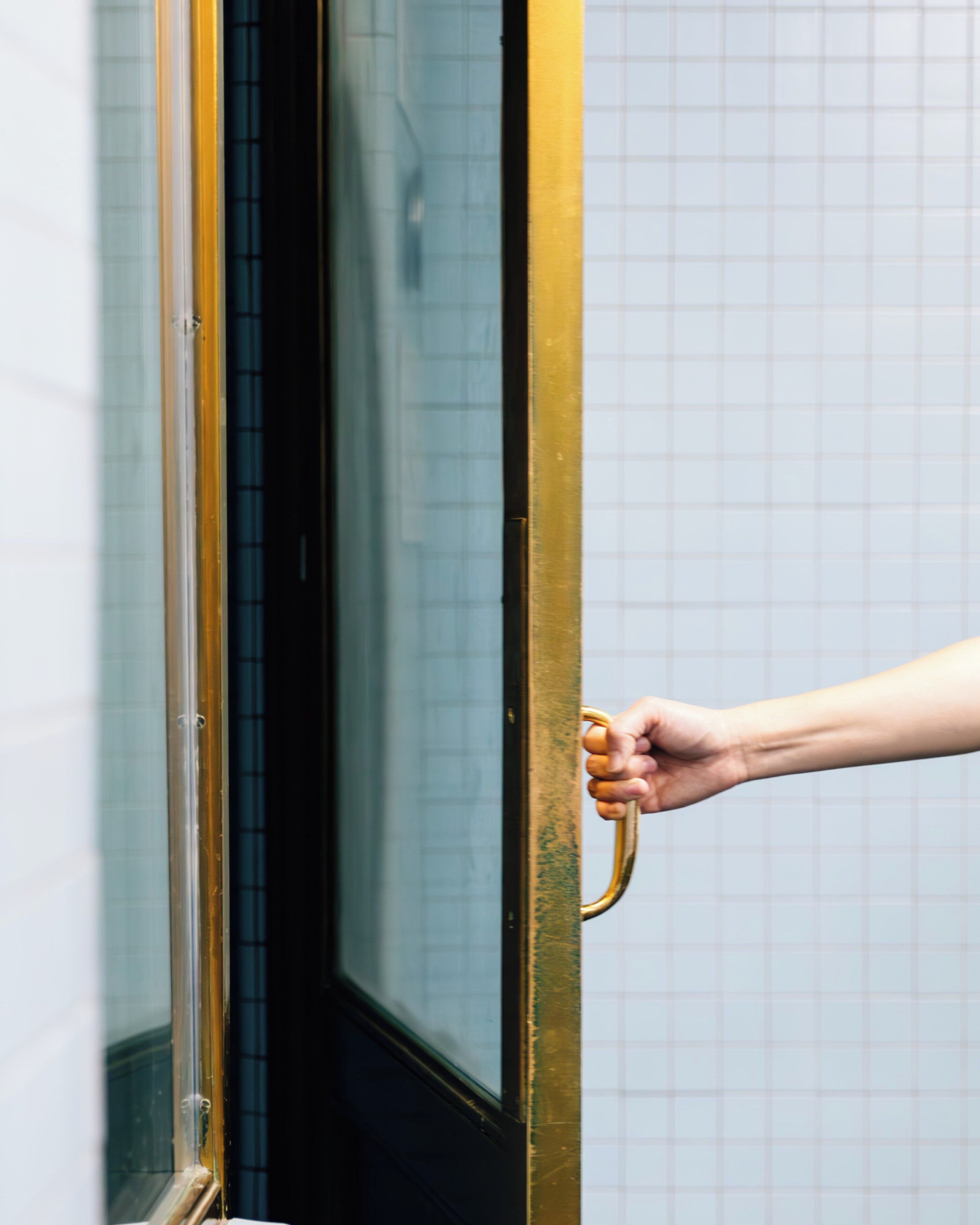 A hand holding a door handle, with a grid-patterned wall in the background.