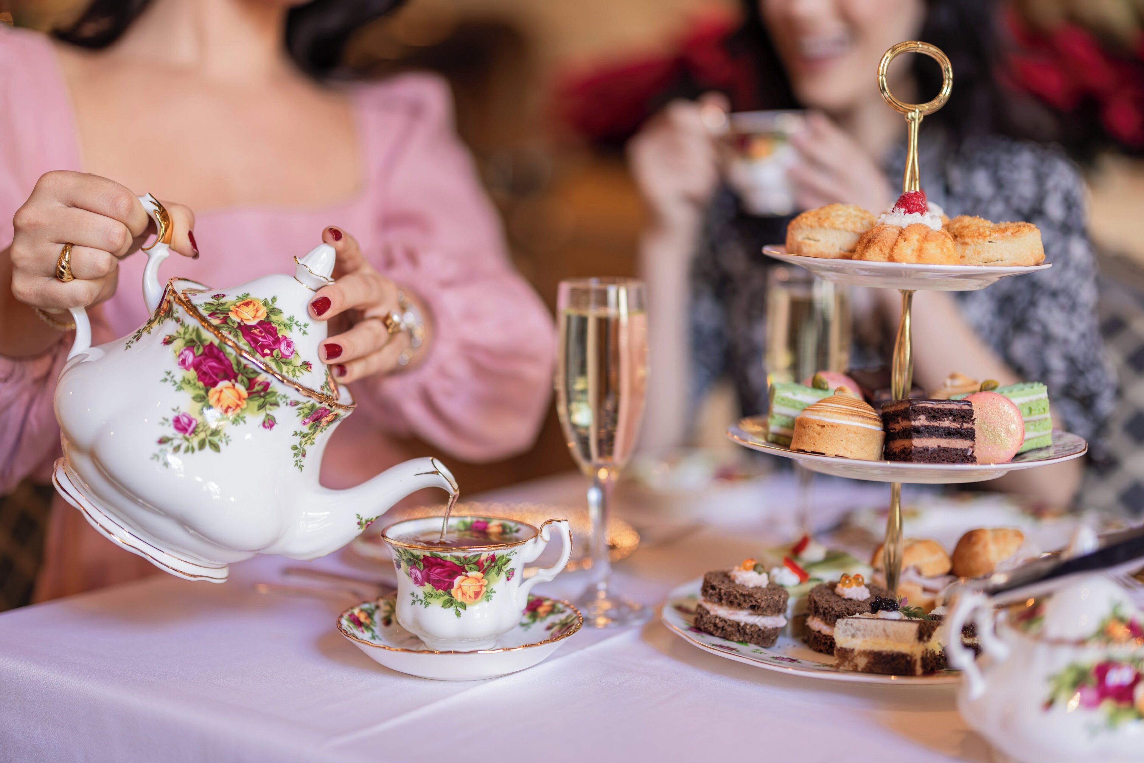A tea service with floral designs, a tiered dessert stand, and a glass of champagne.