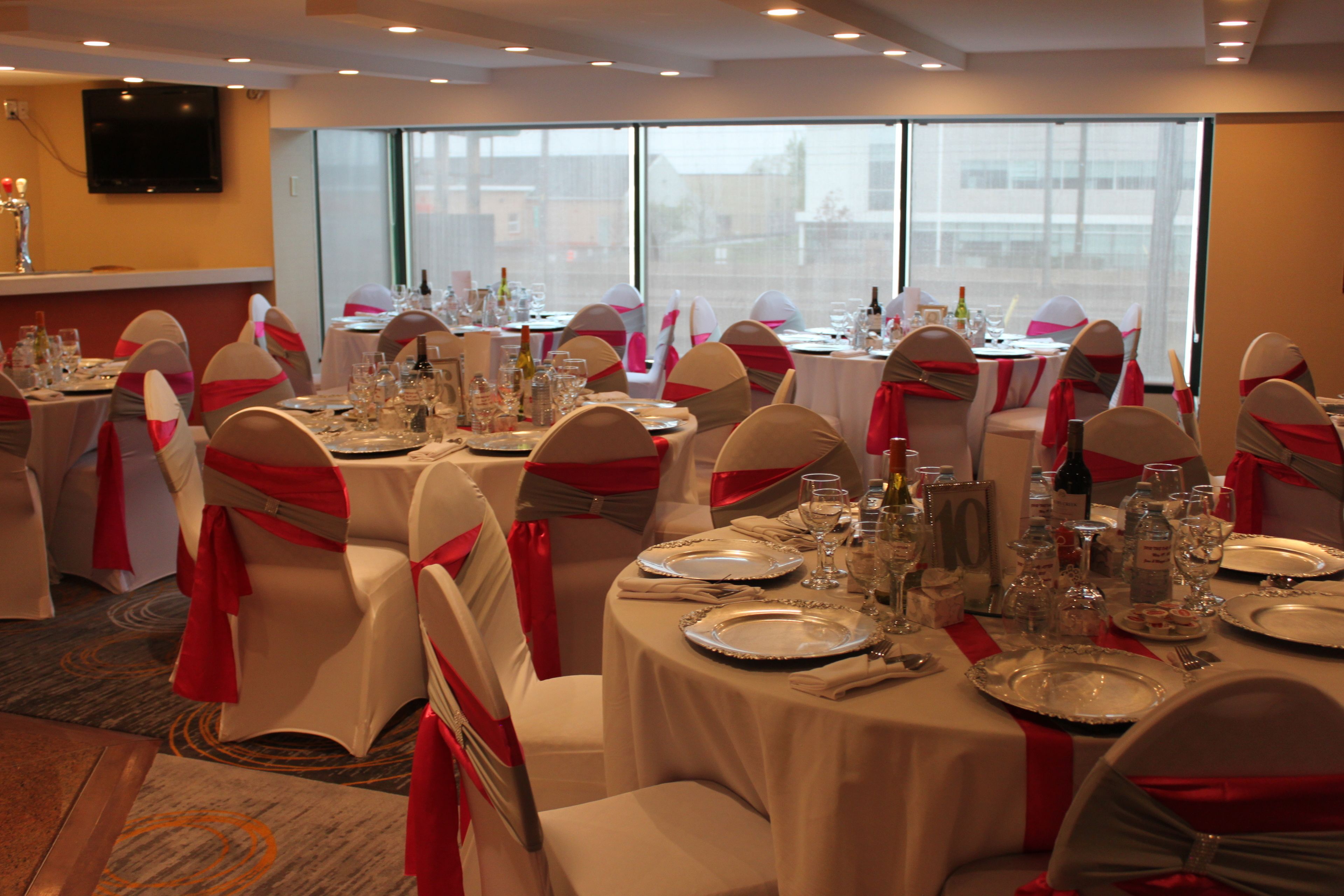 A banquet hall with round tables set for a formal event, each with white tablecloths and red sashes on chairs.