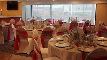 A banquet hall with round tables set for a formal event, each with white tablecloths and red sashes on chairs.