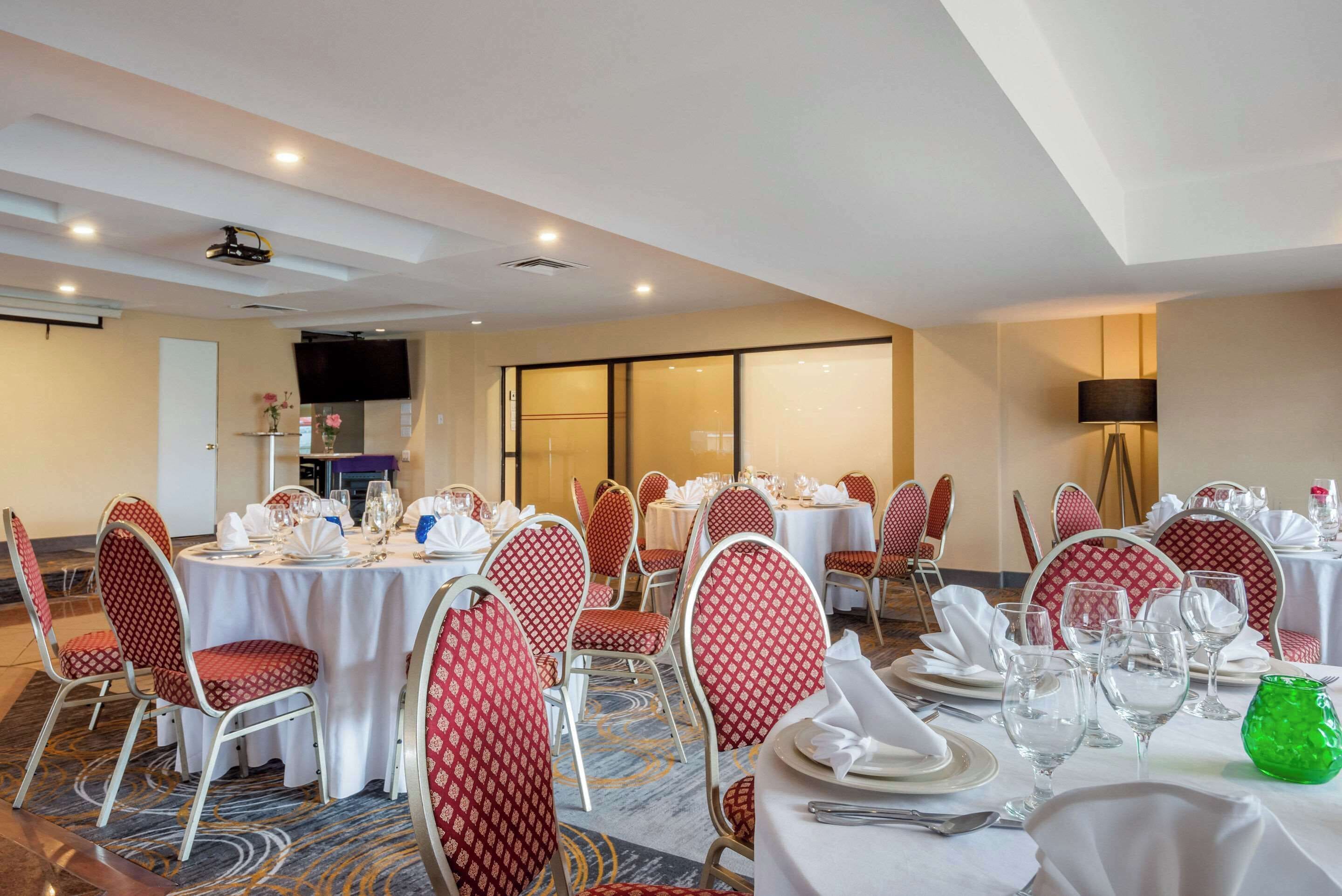 A banquet hall with round tables set for dining, red patterned chairs, and a carpeted floor.