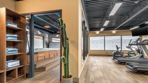 Ein Fitnessstudio mit Holzböden, Trainingsgeräten und einer Säulenkaktus-Pflanze.