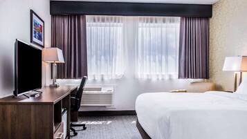 A hotel room with a bed, a desk with a computer, a TV, and a window with curtains.