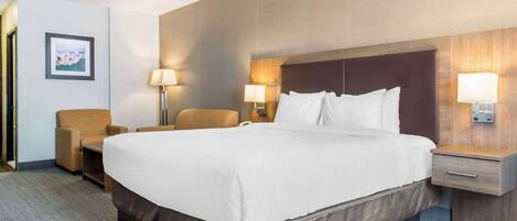 A hotel room with a large bed, two bedside tables with lamps, a chair, and a framed picture on the wall.