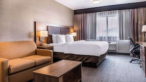 Ein Hotelzimmer mit Bett, Sofa, Schreibtisch, Lampe und einem Fenster mit Vorhängen.