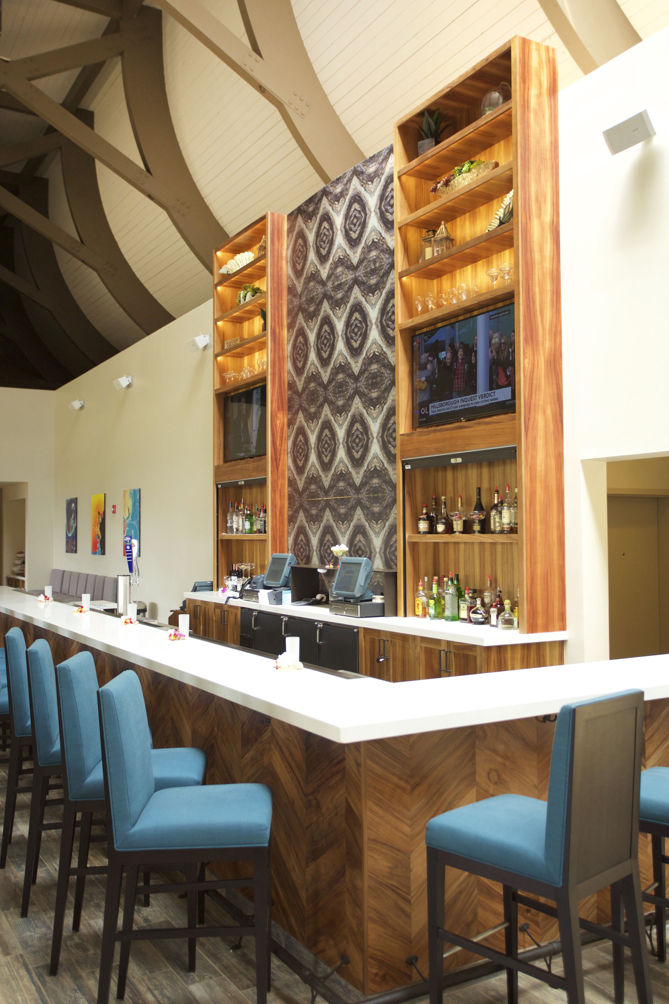 A bar area with a long counter, blue bar stools, and shelves stocked with bottles.