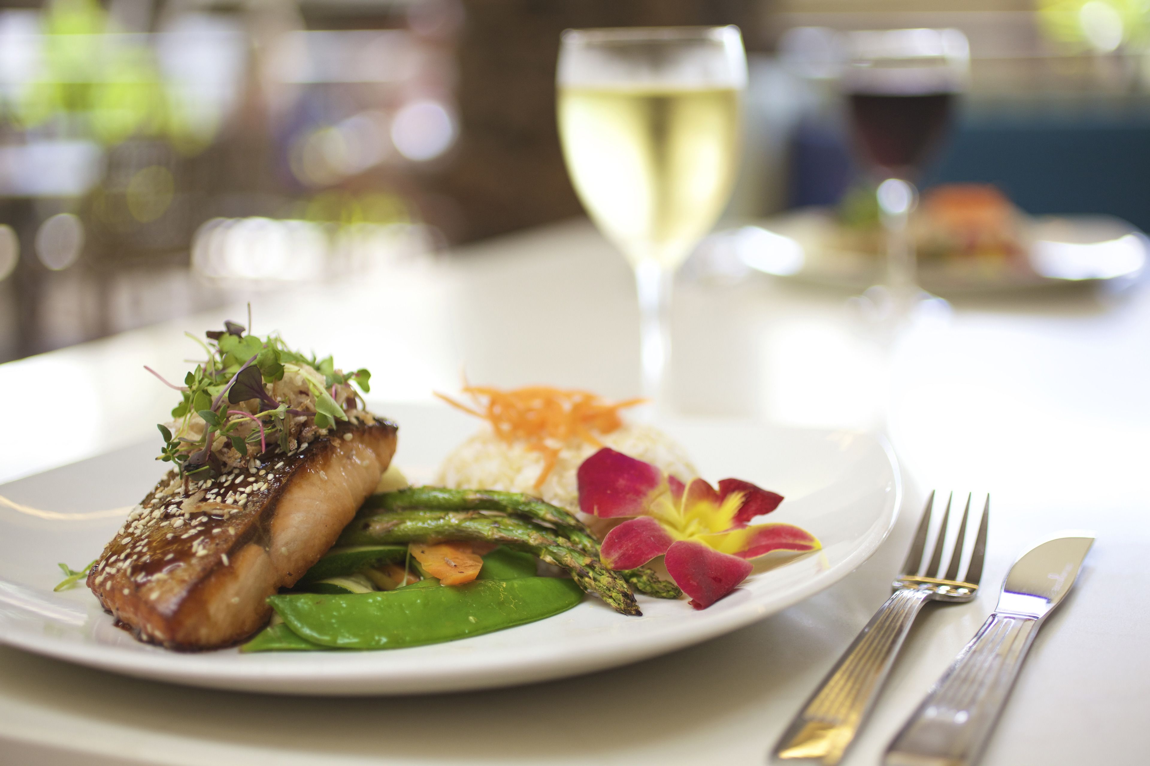 A plate of food with a fish, asparagus, and greens, accompanied by a glass of white wine and a glass of red wine.