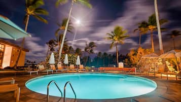 A swimming pool with lounge chairs and umbrellas, surrounded by palm trees and a building.