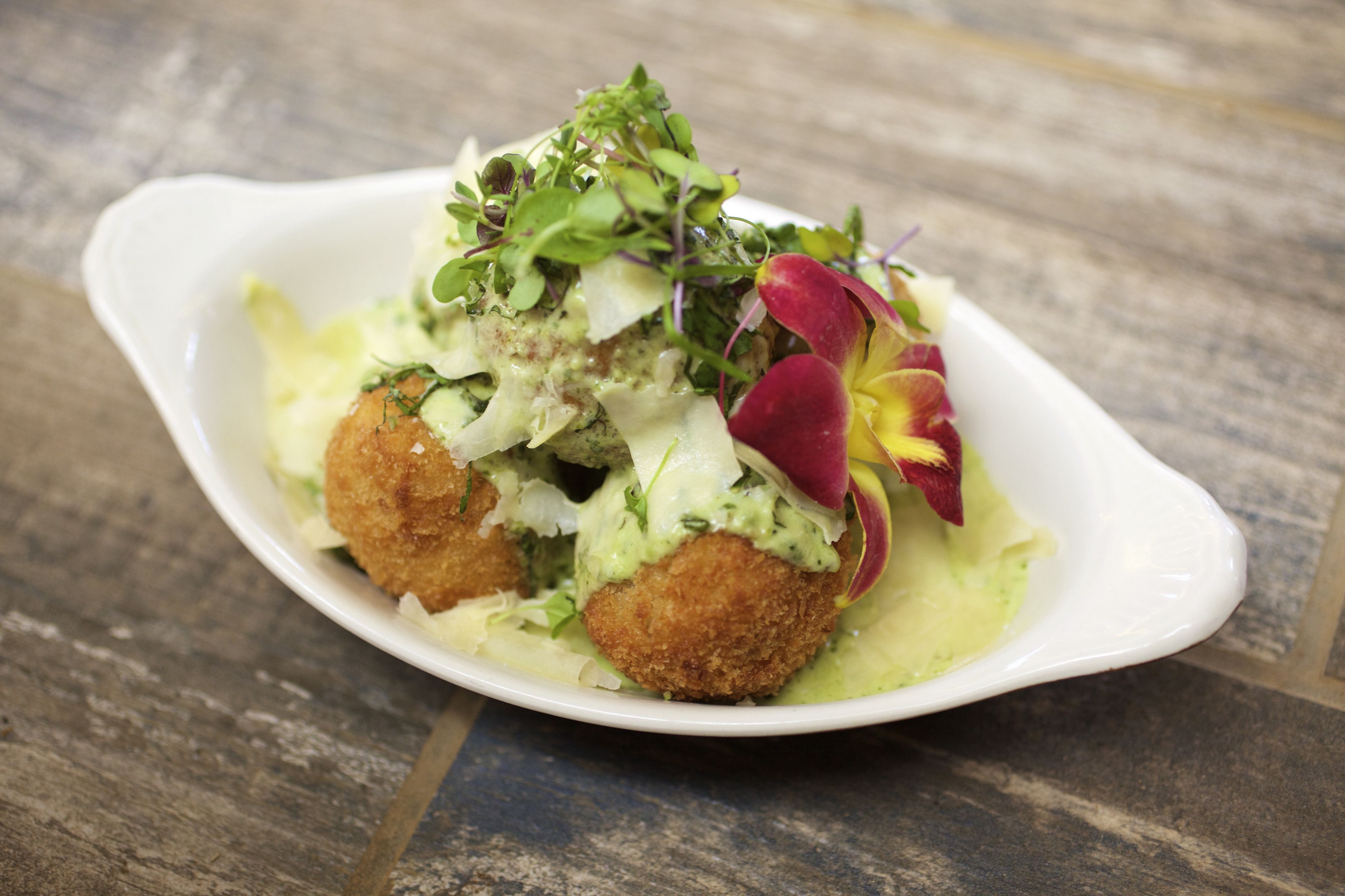 A white oval dish containing a salad with greens, a red flower, and a creamy dressing.