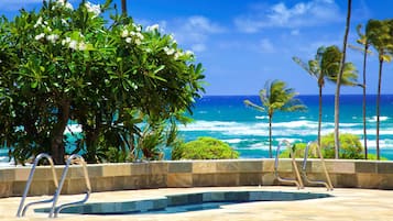 A pool area with a view of the ocean, surrounded by palm trees and a large bush.