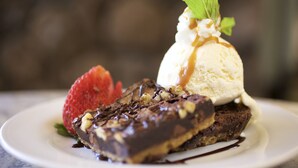 Une assiette de dessert comprenant un brownie au chocolat, une boule de glace à la vanille, une fraise et une feuille de menthe.