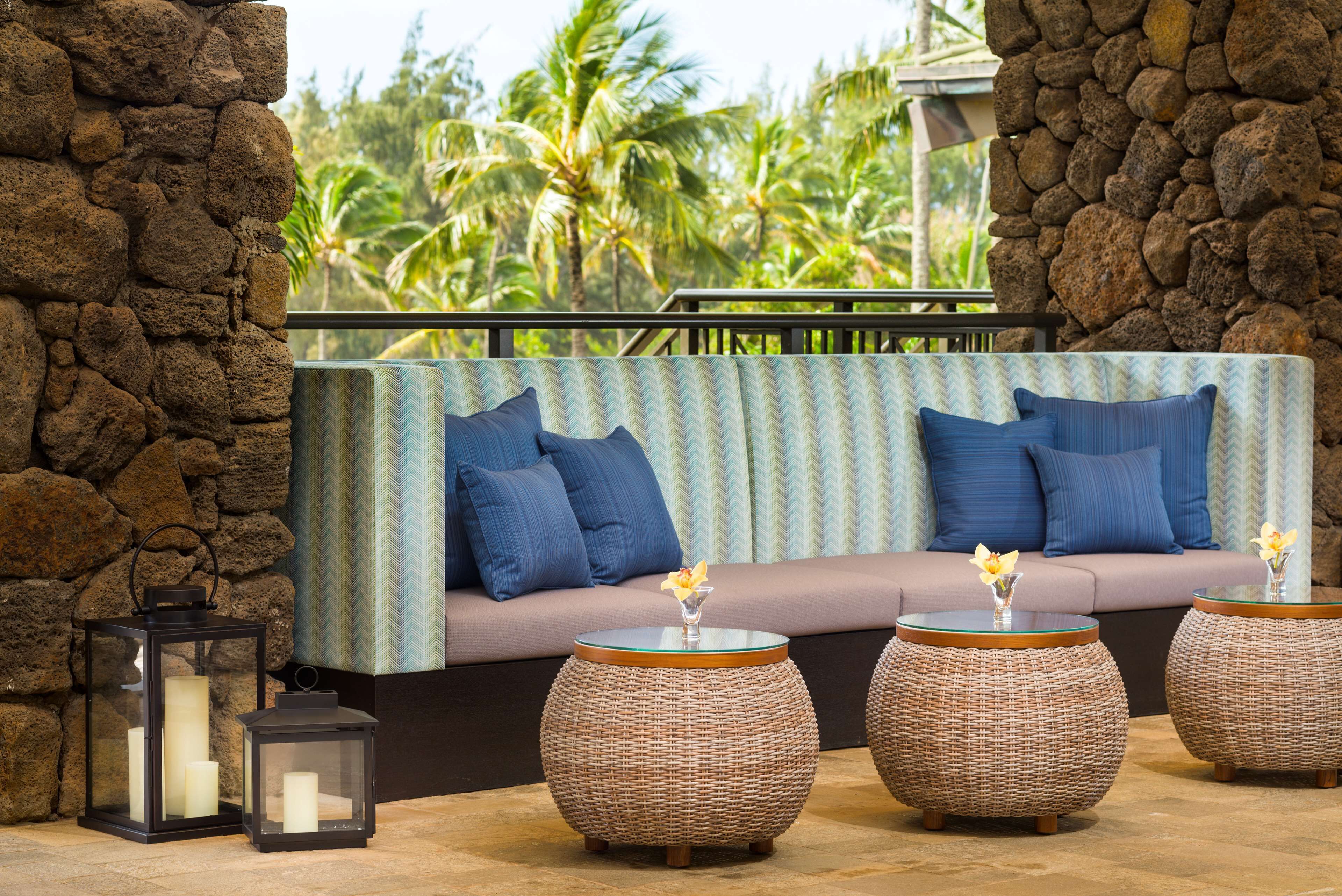 A stone wall, a cushioned seating area with blue cushions, and wicker tables with candles and flowers.