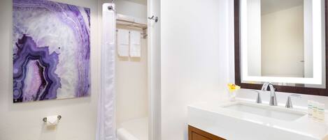 A bathroom with a white sink, a mirror, a shower curtain, and a marble wall art piece.