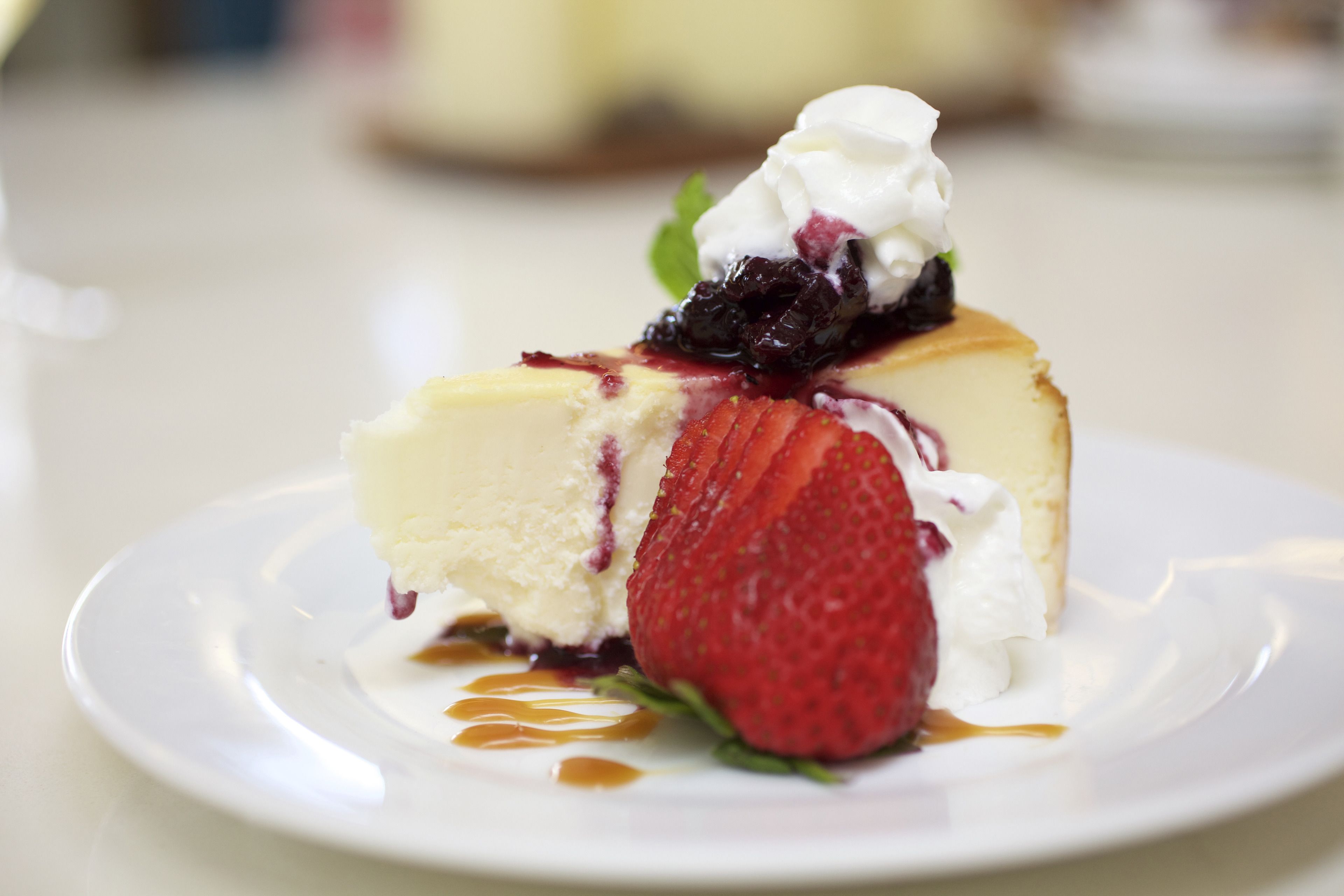 Una porción de pastel de queso con crema batida y una fresa sobre un plato blanco.