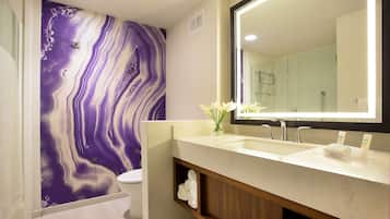 Un baño moderno con pared de mármol, un espejo grande, un lavamanos y un inodoro.