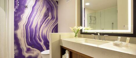 Un baño moderno con pared de mármol, un espejo grande, un lavamanos y un inodoro.