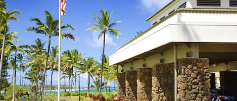 A modern building with a stone facade, a flagpole with a flag, and a view of the ocean.