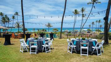 Un área de comedor al aire libre con mesas y sillas, con vistas a una playa y al océano.