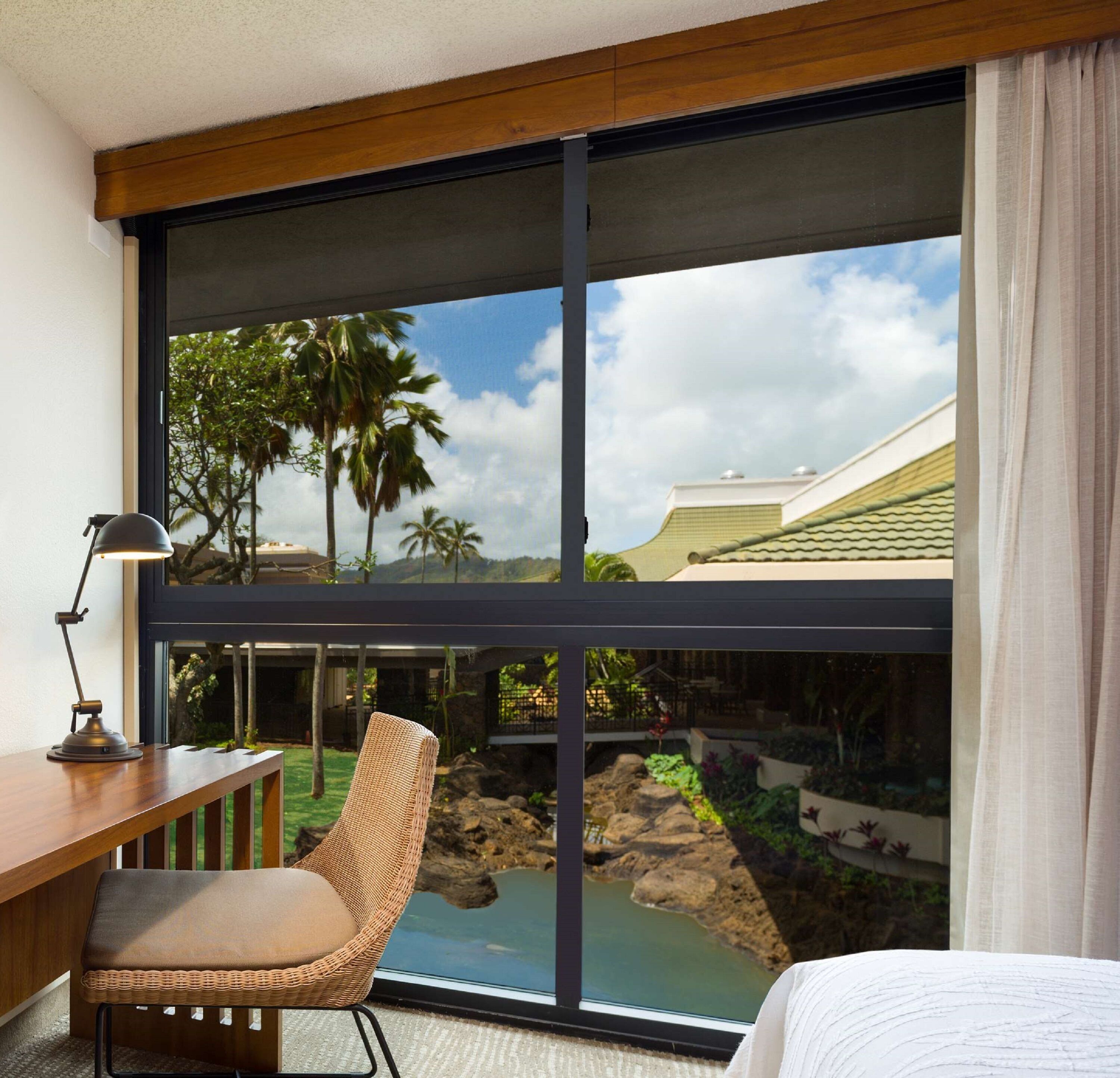 A hotel room with a large window, a desk, a chair, and a bed.