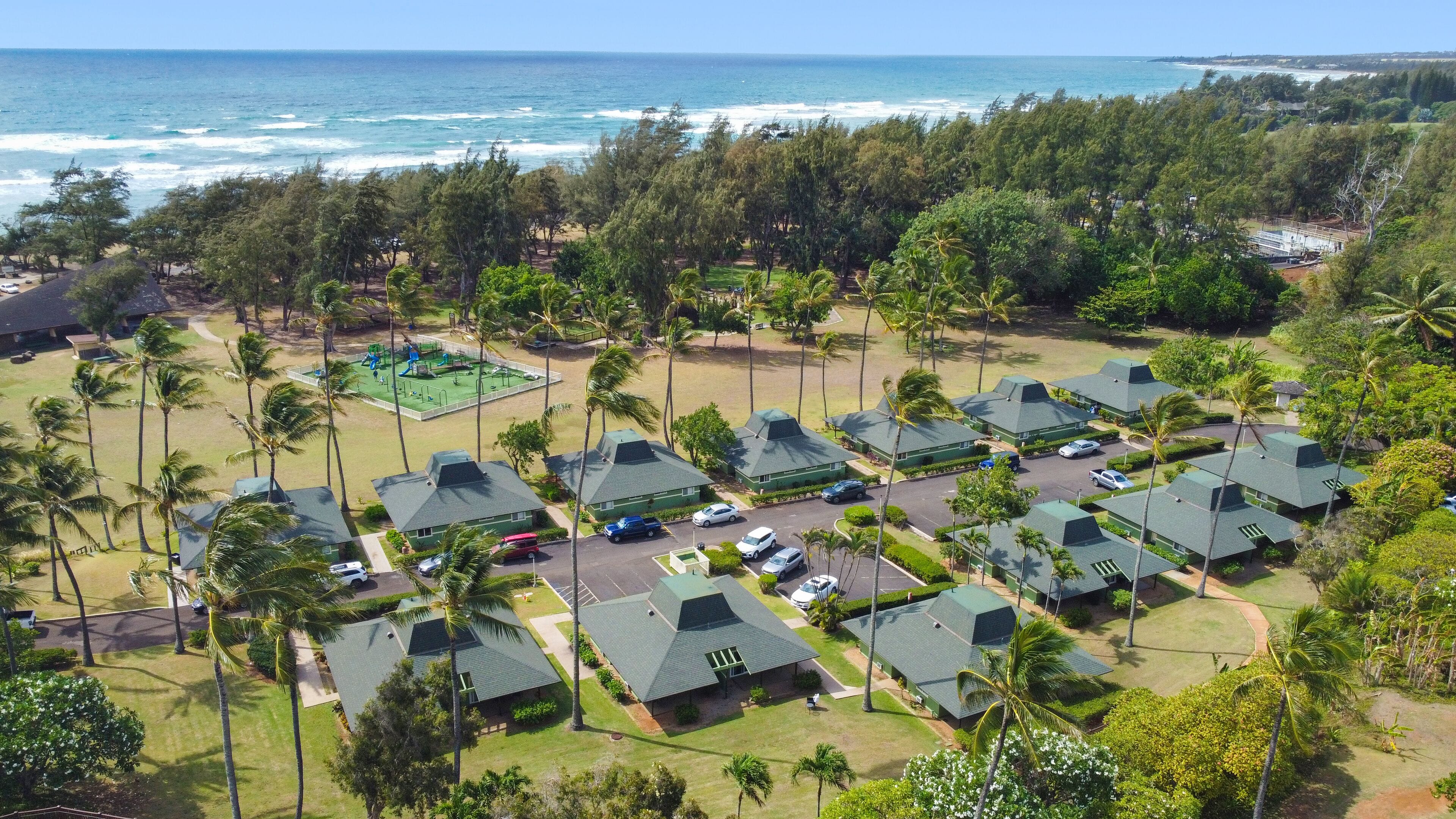 A resort with multiple green-roofed buildings, a playground, and a view of the ocean.