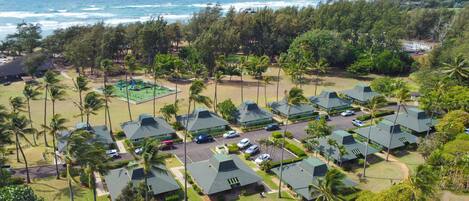 Um resort com vários edifícios com telhados verdes, um parquinho e vista para o oceano.