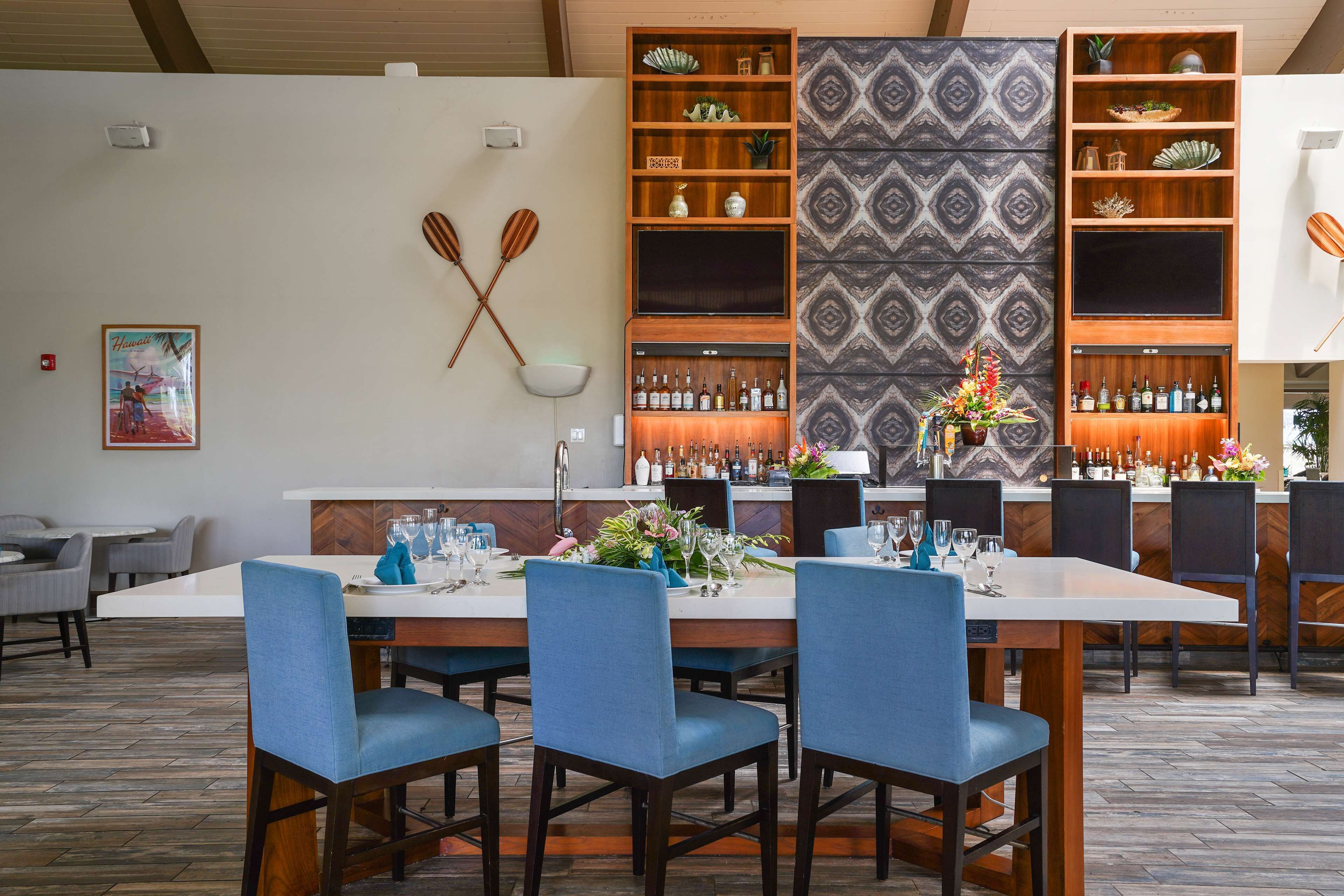 A restaurant with a long counter, blue upholstered chairs, and a bar area with shelves of bottles.