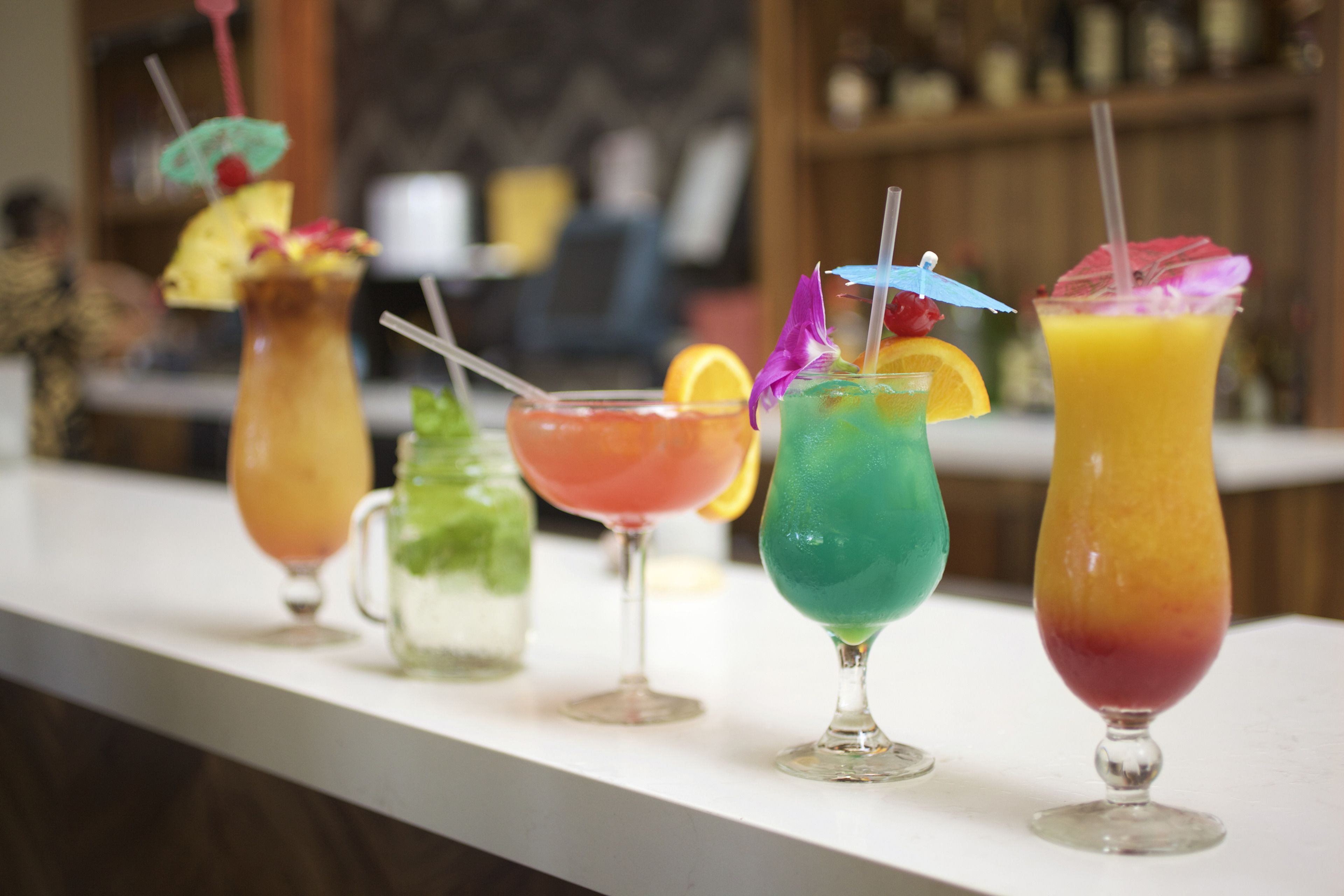 Una barra con una variedad de cócteles coloridos, cada uno decorado con diferentes frutas y pajitas.