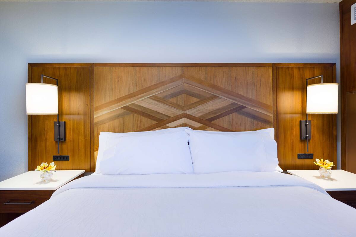 A hotel room with a large bed, two bedside tables with lamps, and a wooden headboard with a geometric pattern.