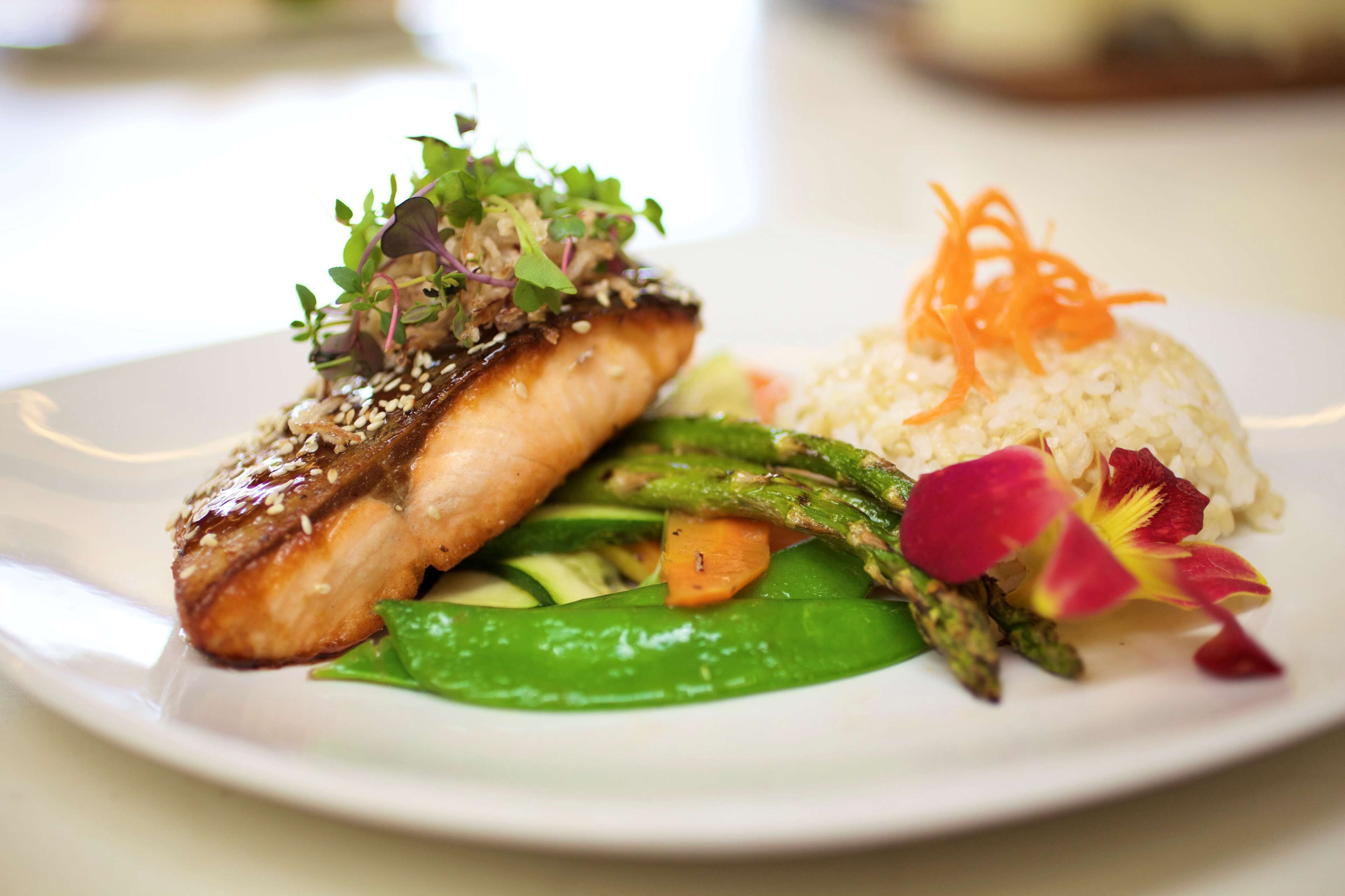 A plate with grilled salmon, asparagus, and rice garnished with microgreens and carrot shreds.