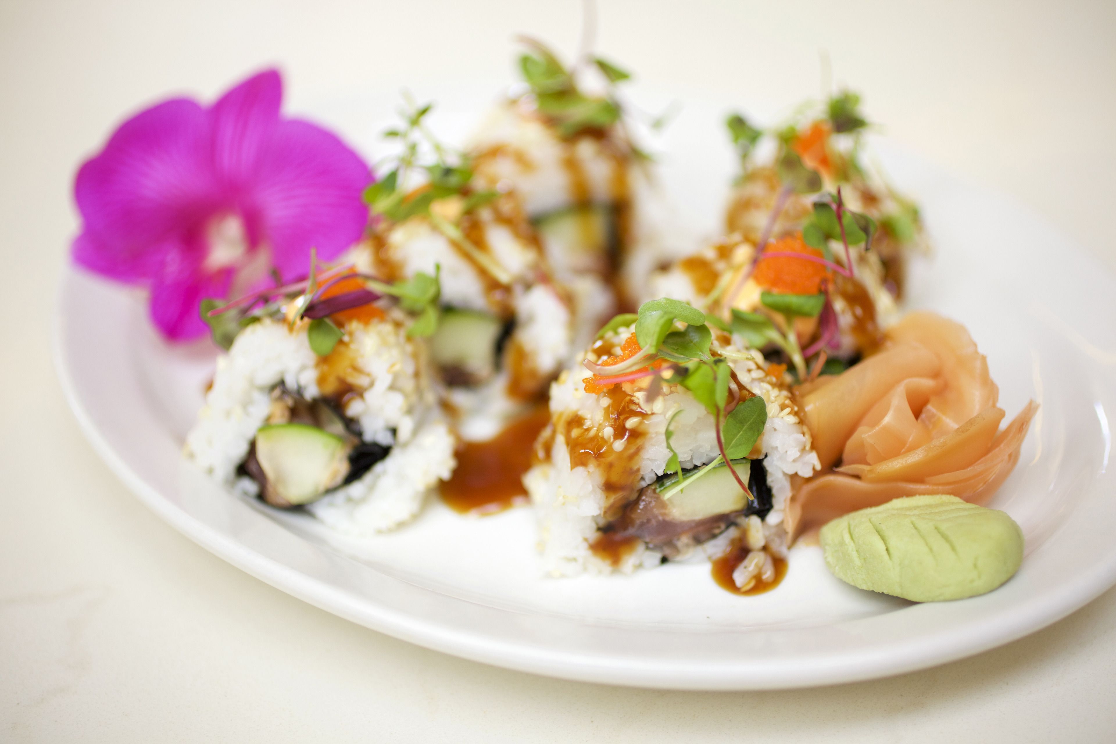 Een bord sushi met een paarse bloem en een klein beetje wasabi.