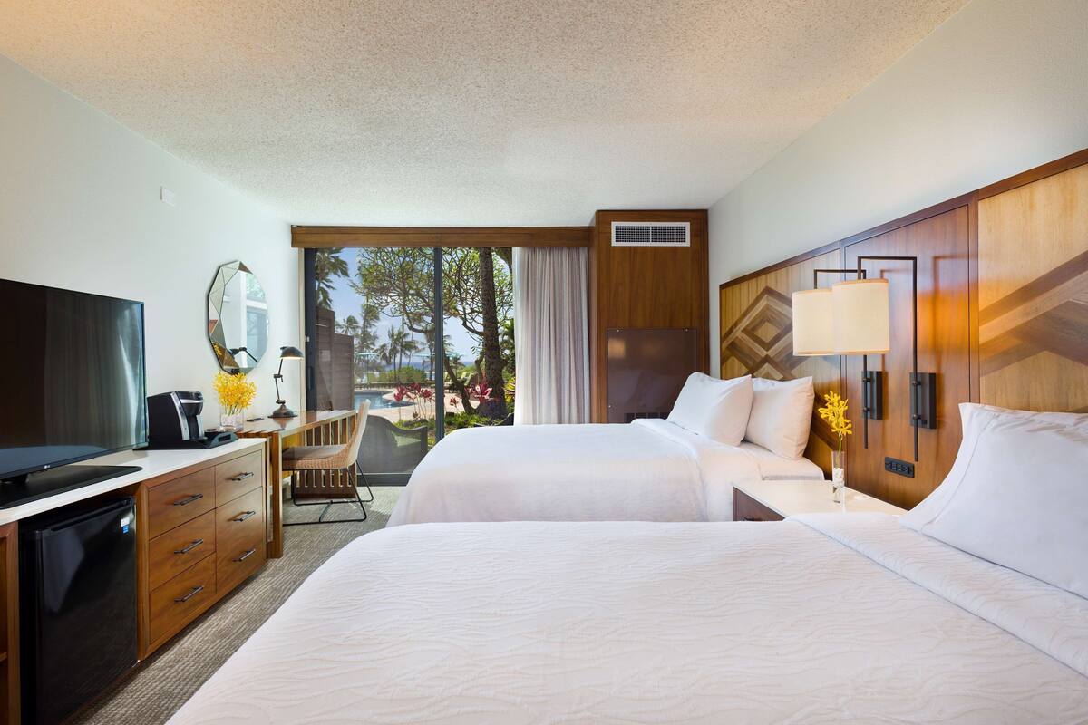 A hotel room with a bed, a desk with a TV, a chair, a window with a view, and a lamp.