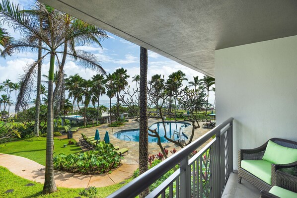 A balcony with a view of a pool, palm trees, and a grassy area.