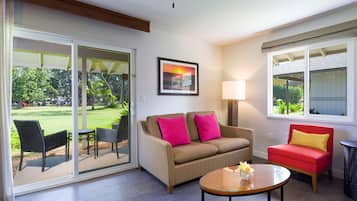 A living room with a sliding glass door leading to a patio, a beige sofa with pink cushions, a red armchair, a wooden coffee table, and a lamp.
