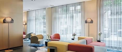 Un lobby de hotel moderno con zona de estar, ventanas amplias y lámparas decorativas.
