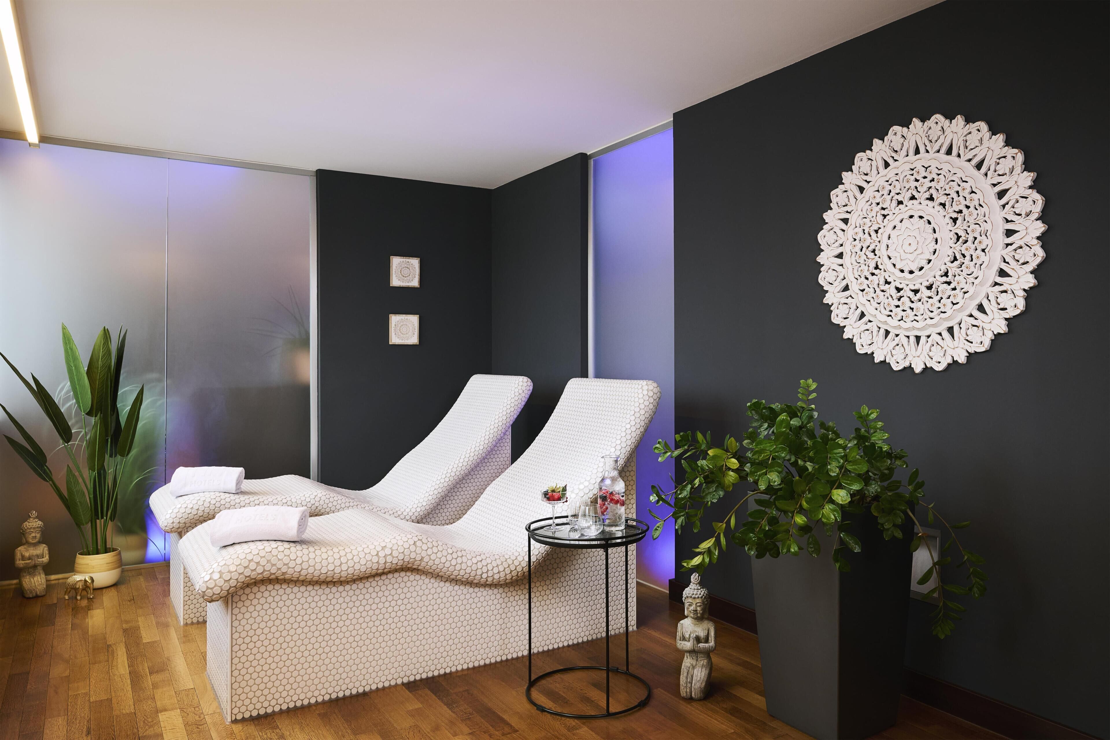 A spa room with two reclining chairs, a small table with a glass, and a decorative wall piece.