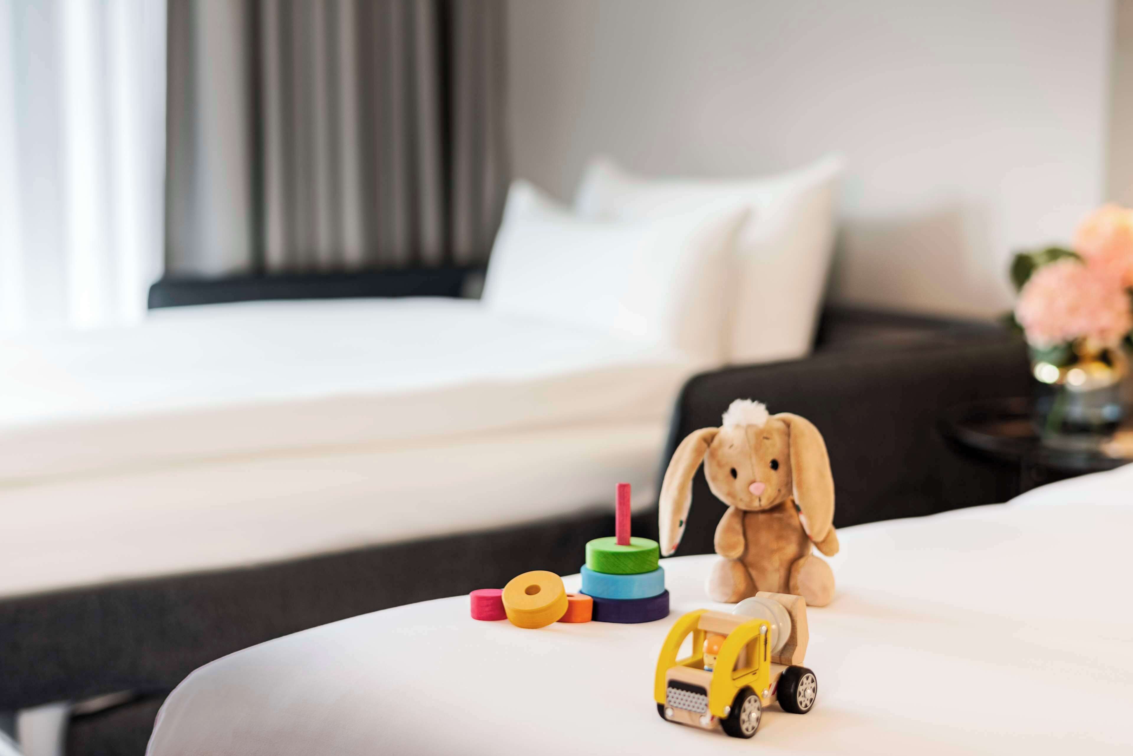 Hotellihuone, jossa on siististi pedattu sänky, pieni leluauto, pehmojänis ja sängyllä värikäs pino renkaita.