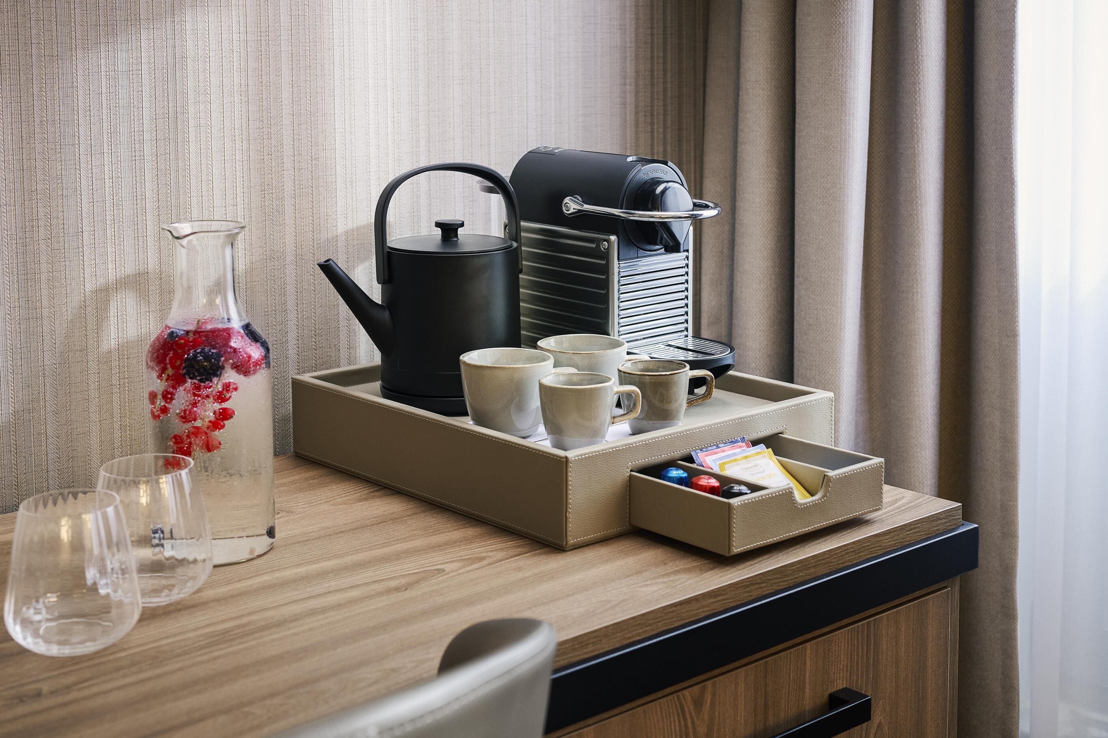 Una mesa de madera con un florero de vidrio lleno de bayas, una tetera, tazas y una bandeja con cafetera y una caja de pañuelos.