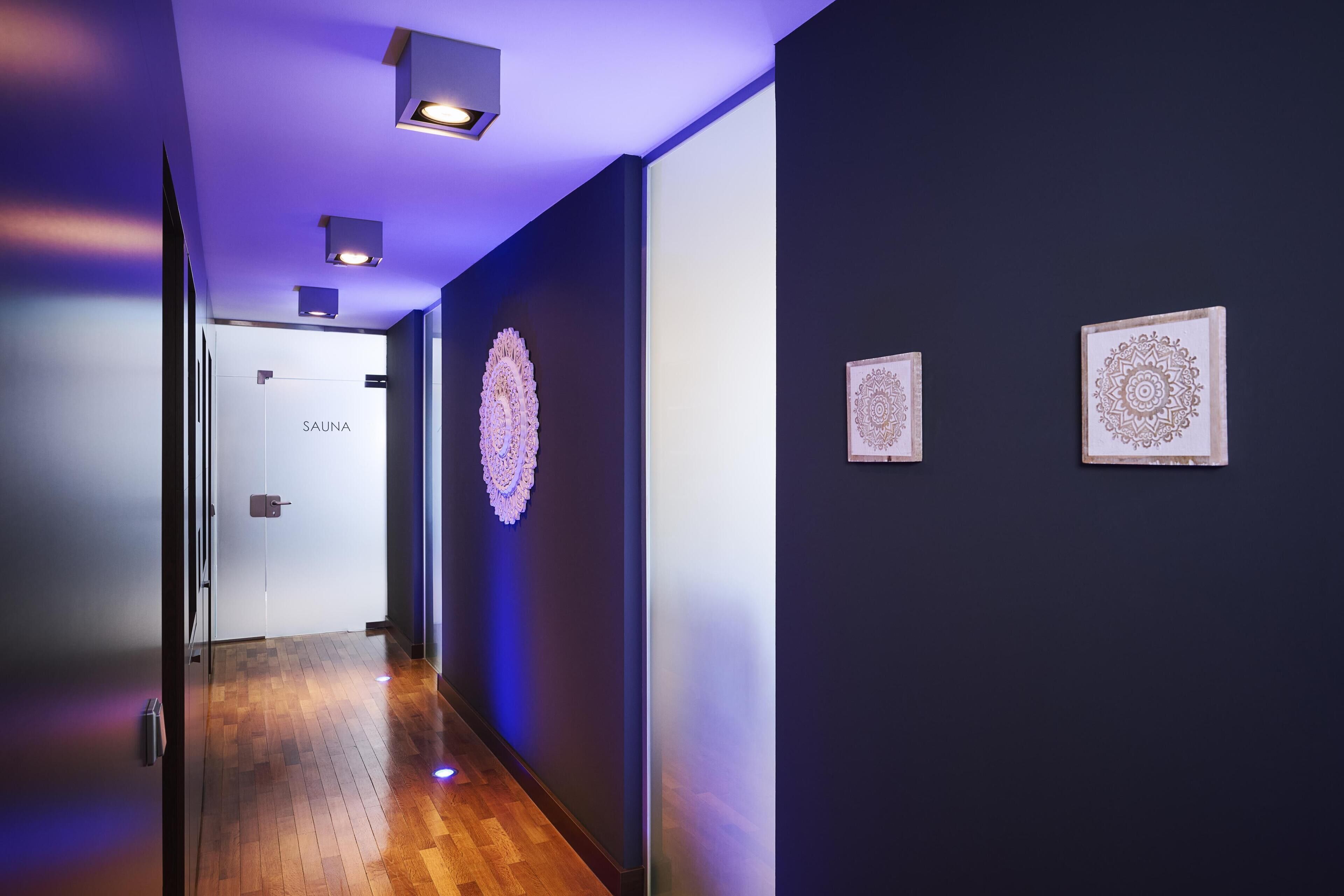 A hallway with a wooden floor, a door labeled 'SAUNA', and two wall-mounted decorative items.