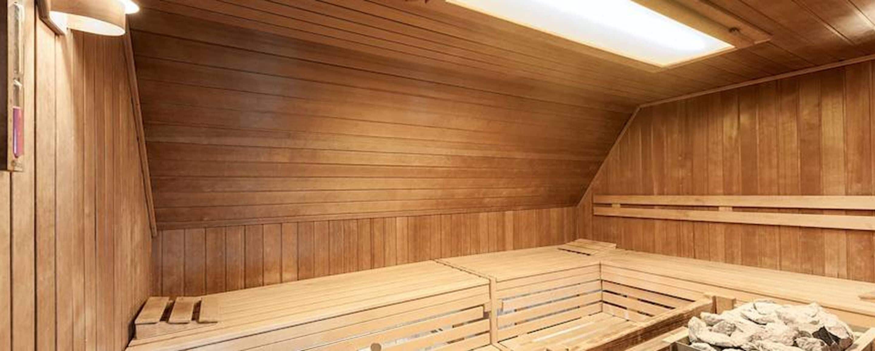 Un sauna avec des bancs en bois, un éclairage au plafond et un mur en bois.