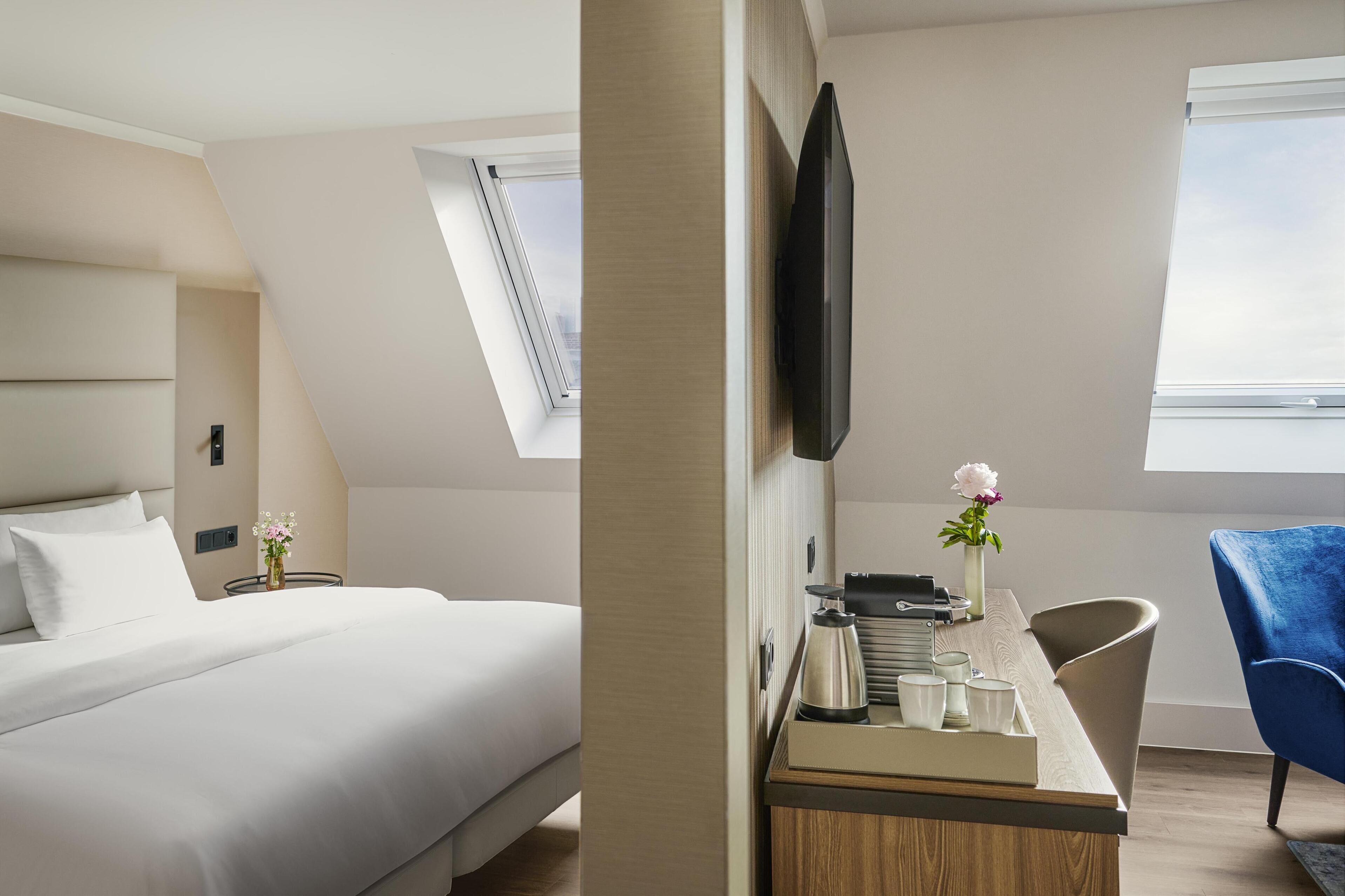 Et moderne hotelværelse med en seng, et skrivebord med elkedel, en stol, et fjernsyn og et vindue med udsigt.