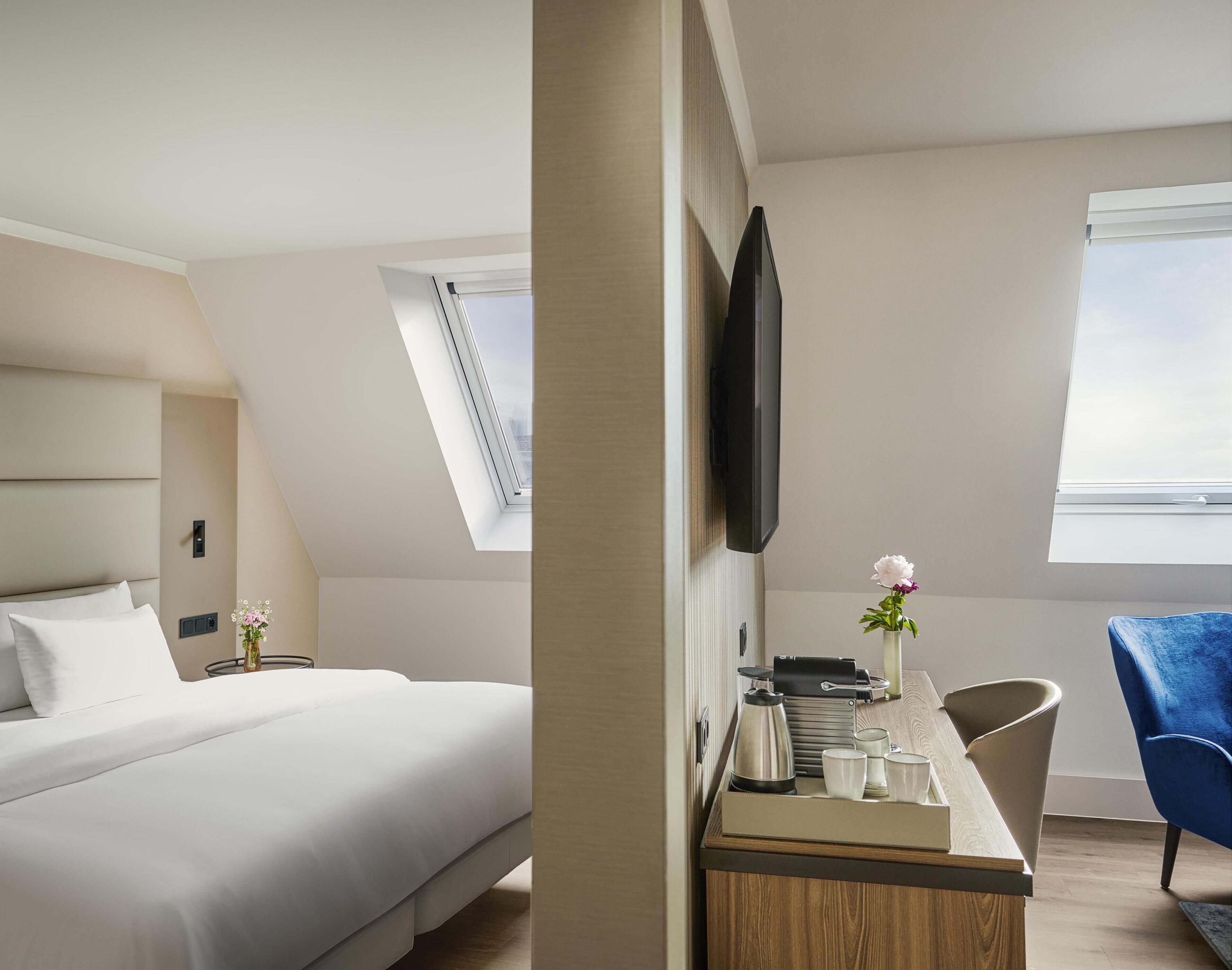 A modern hotel room with a bed, a desk with a flat-screen TV, a chair, and a window with a view.