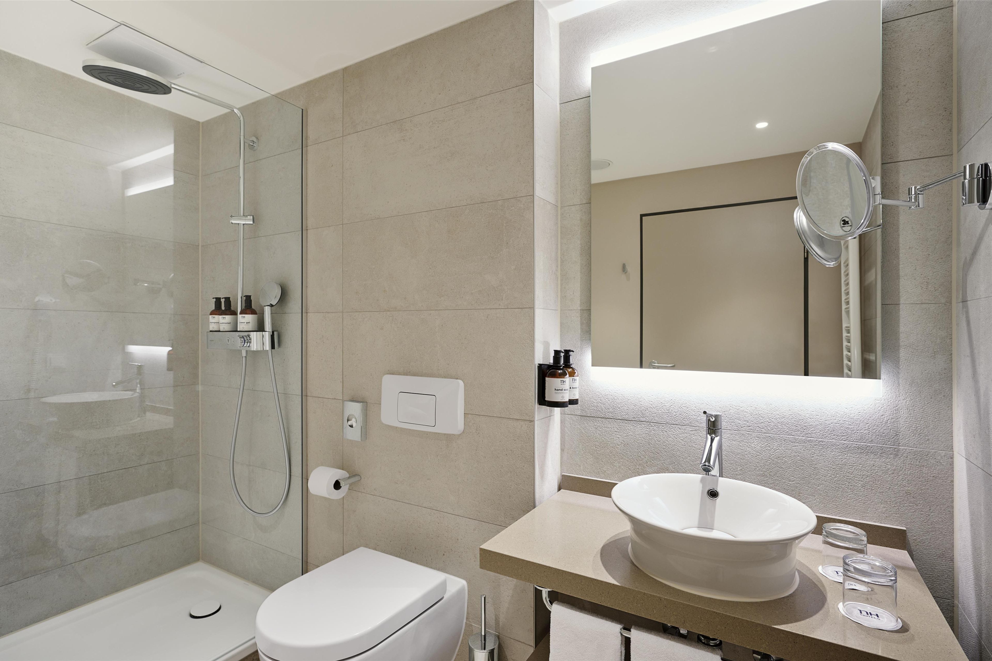 A modern bathroom with a glass-enclosed shower, a white toilet, a beige sink with a mirror, and a towel rack.