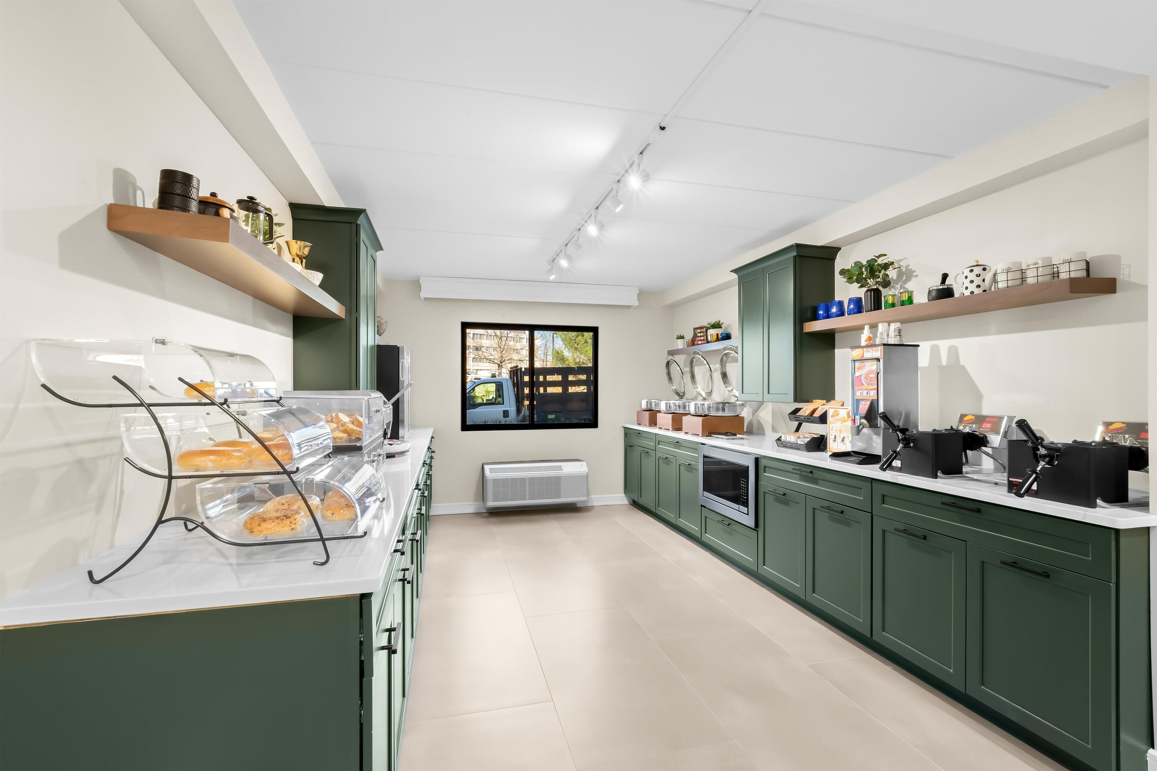 A modern kitchen with green cabinets, a marble countertop, and a built-in oven.