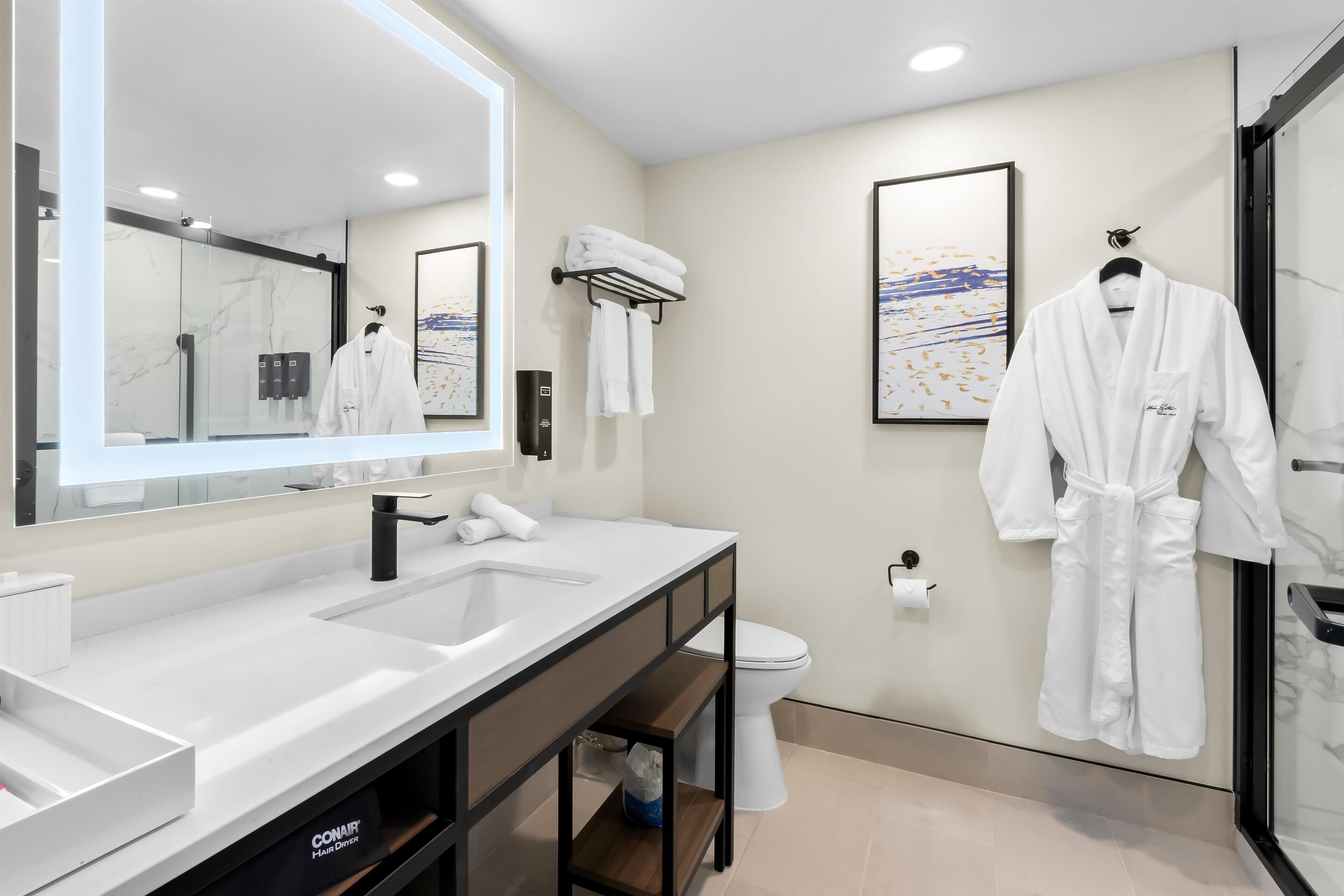 A modern bathroom with a large mirror, dual sinks, a toilet, and a glass shower enclosure.