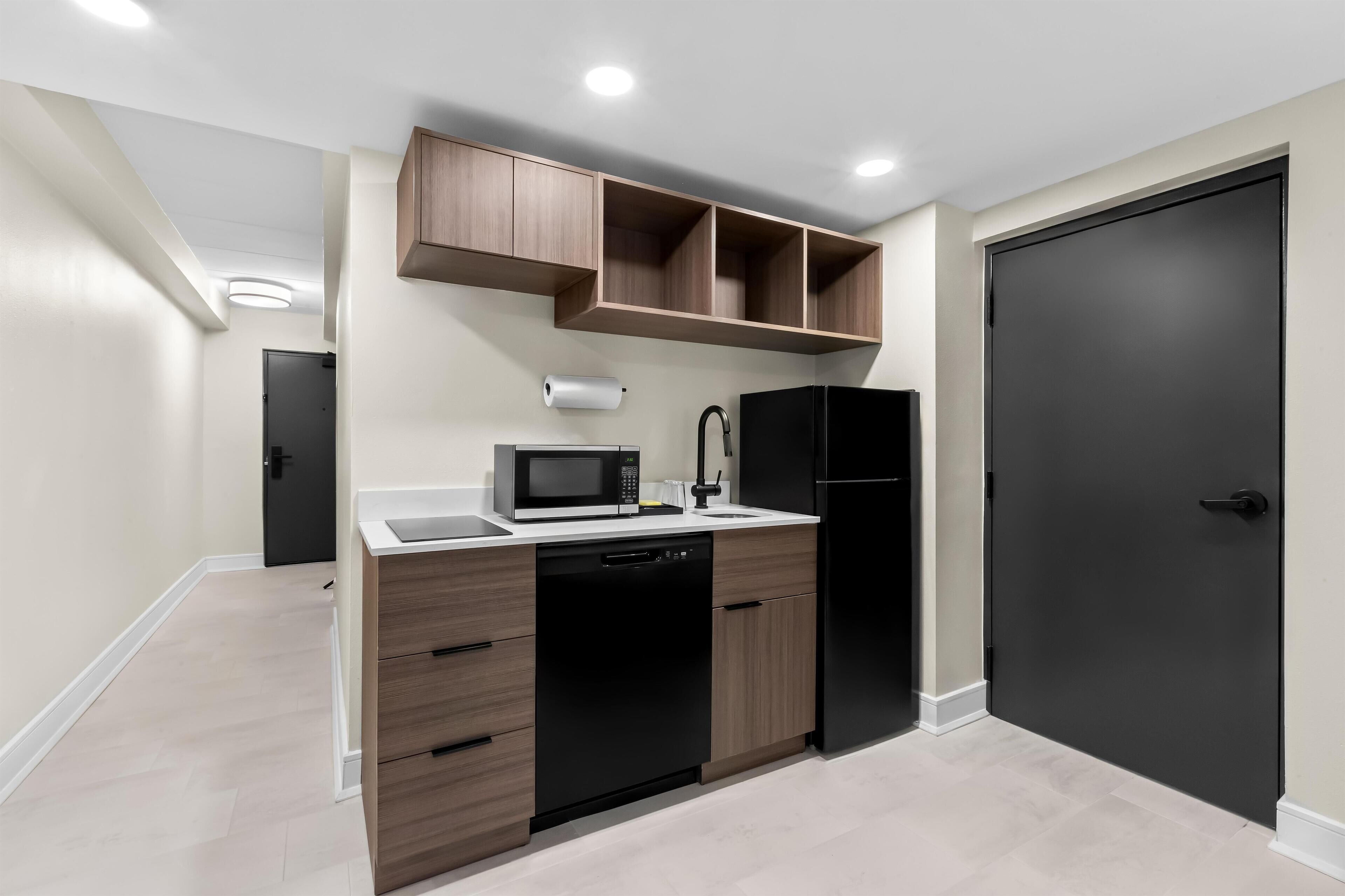 A compact kitchen with a microwave, dishwasher, and black refrigerator.
