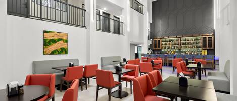 Un moderno vestíbulo de hotel con varias zonas de estar, un bar y una escalera.